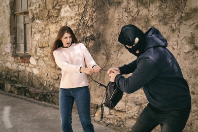 Masked man trying to steal woman's backpack outdoors. Criminal offence
