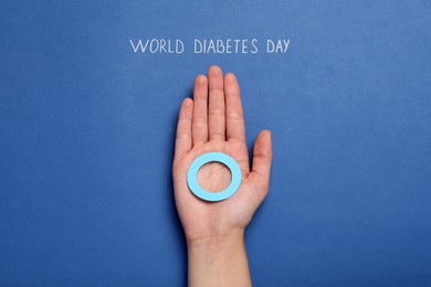 Woman holding blue paper circle near text World Diabetes Day on color background, top view