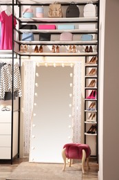 Modern mirror near storage rack with stylish clothes, shoes and accessories in wardrobe room. Interior design