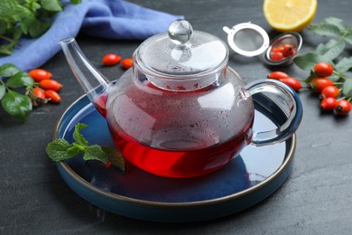 Teapot with aromatic rose hip tea and fresh mint on black table