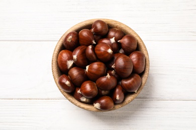 Fresh sweet edible chestnuts on white wooden table, top view
