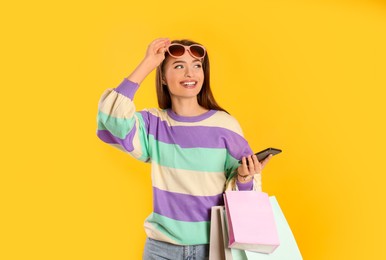 Happy young woman with shopping bags and smartphone on yellow background. Big sale