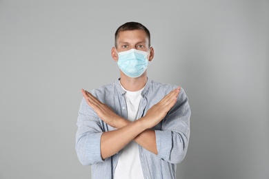 Man in protective mask showing stop gesture on grey background. Prevent spreading of coronavirus