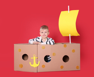 Little child playing with ship made of cardboard box on red background