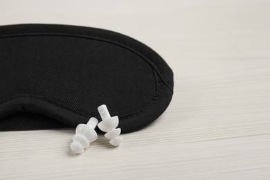 Pair of ear plugs and sleeping mask on white wooden background