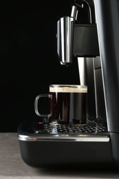Photo of Modern espresso machine with glass cup of coffee on grey table against black background