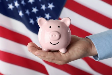 Woman holding piggy bank against American flag, closeup