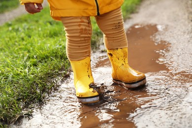 Little girl wearing rubber boots walking in puddle, closeup