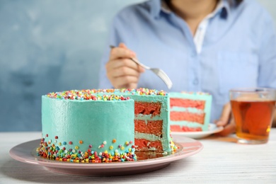 Cut fresh delicious birthday cake and blurred woman on background