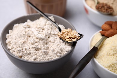 Bowls with different types of flour and ingredients on light grey table, closeup