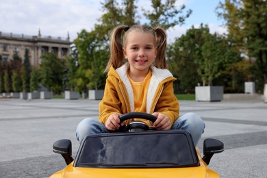 Photo of Cute little girl driving children's car on city street