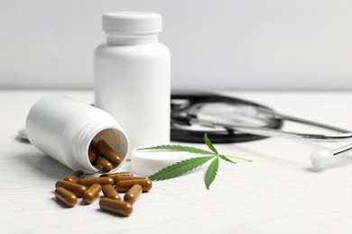 Hemp leaf, bottles with capsules and stethoscope on white wooden table