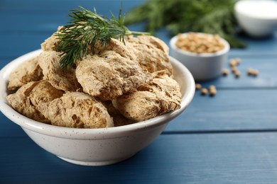Dehydrated soy meat chunks with dill in bowl on blue wooden table, closeup