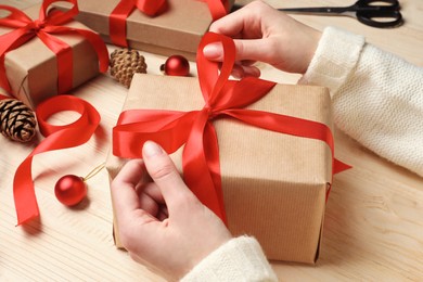 Christmas present. Woman tying ribbon bow on gift box at wooden table, closeup