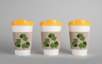 Carton cups with recycling symbols on grey background
