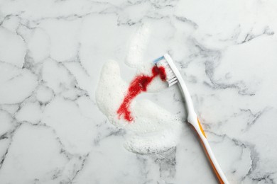 Brush and toothpaste foam with blood on white marble table, top view. Gum problems