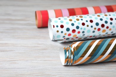 Different colorful wrapping paper rolls on white wooden table, closeup. Space for text