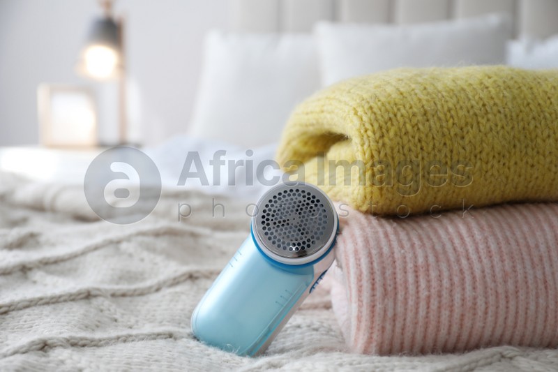 Photo of Modern fabric shaver and woolen sweaters on bed indoors, closeup. Space for text