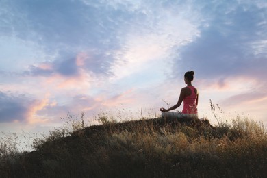 Woman meditating on hill near sea, back view. Space for text