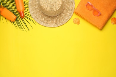 Beach towel, straw hat, sunglasses and sun protection products on yellow background, flat lay. Space for text