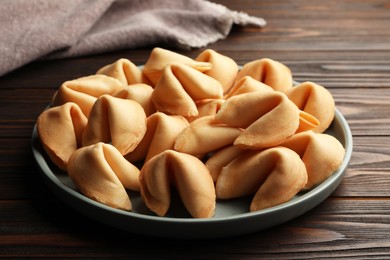 Photo of Tasty fortune cookies with predictions in plate on wooden table, closeup