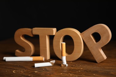 Broken and whole cigarettes near word Stop on wooden table. Quitting smoking concept