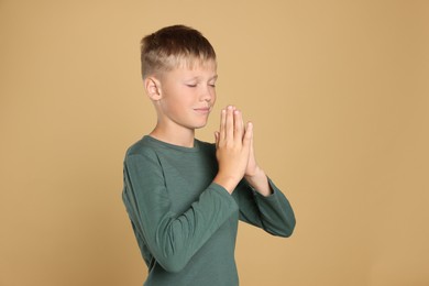 Boy with clasped hands praying on beige background