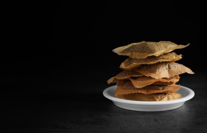 Saucer with used tea bags on dark table against black background. Space for text