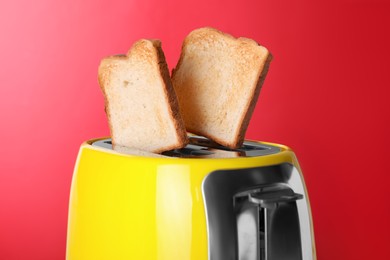 Yellow toaster with roasted bread against red background, closeup