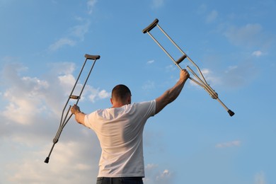 Man raising hands with underarm crutches up to sky outdoors, back view. Healing miracle