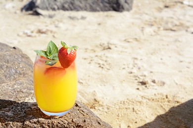Photo of Glass of refreshing drink with strawberry on beach, space for text