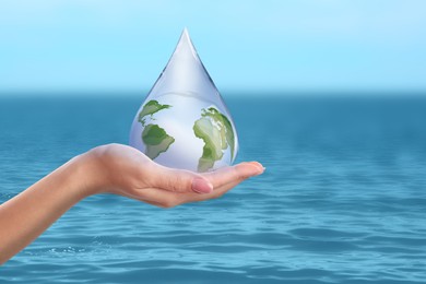 Woman holding icon of Earth in drop near ocean, closeup. Water save concept