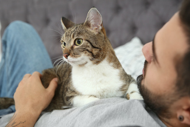 Man with cat on bed at home, closeup. Friendly pet
