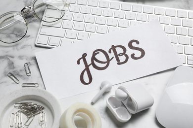 Photo of Card with word JOBS, computer keyboard, earphones and stationery on white marble table. Career concept