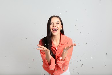 Emotional woman and falling confetti on light grey background