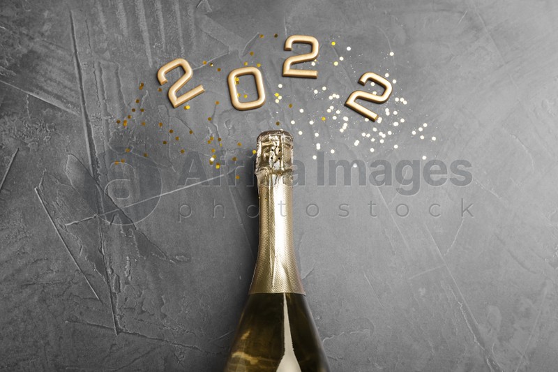 Bottle of sparkling wine, gold confetti and number 2022 on grey background, flat lay. Happy New Year