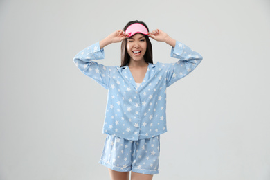 Beautiful Asian woman wearing pajamas and sleeping mask on light grey background. Bedtime