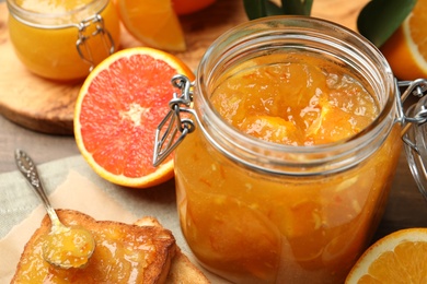 Delicious orange marmalade in jar, fresh fruits and toasts on table, closeup