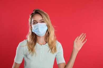 Woman in protective face mask showing hello gesture on red background. Keeping social distance during coronavirus pandemic