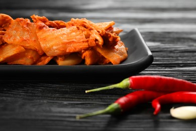 Delicious kimchi with Chinese cabbage, red chili peppers and garlic on black wooden table, closeup