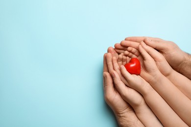 Photo of Parents and kid holding red heart in hands on light blue background, top view. Space for text