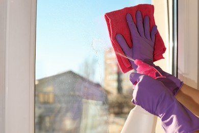 Young woman cleaning window glass with rag and detergent at home, closeup. Space for text