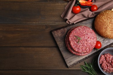 Raw hamburger patties with rosemary and tomatoes on wooden table, flat lay. Space for text