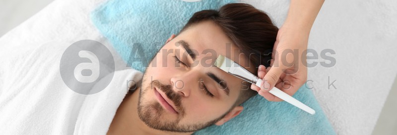Cosmetologist applying mask on client's face in spa salon, above view. Banner design