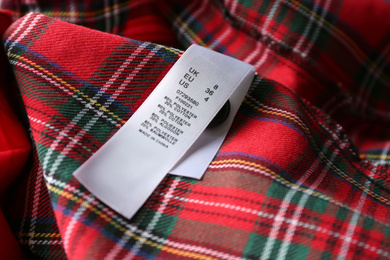 Clothing label with size and content information on red plaid garment, closeup