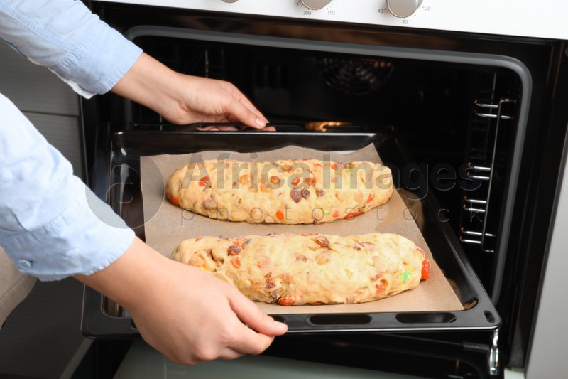 Woman putting baking tray with raw homemade Stollens into oven, closeup. Traditional German Christmas bread