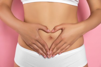 Photo of Woman in underwear making heart with hands on her belly against pink background, closeup. Healthy stomach