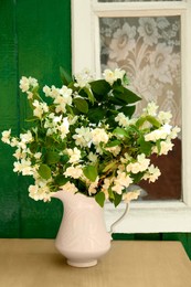 Bouquet of beautiful jasmine flowers in vase on wooden table near window outdoors