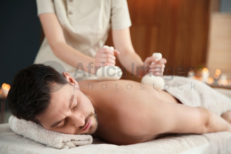 Photo of Handsome man receiving herbal bag massage in spa salon