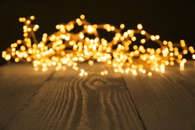 Beautiful glowing Christmas lights on wooden surface, blurred view